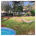 Hammock on a stand in a backyard with a pool and trees in the background