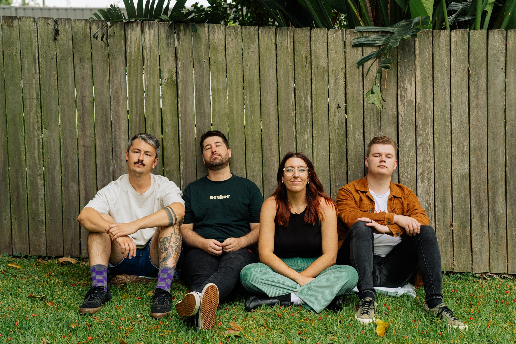 Four people sitting on grass in front of a wooden fence