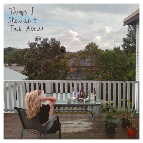 Person sitting on a deck with a glass table, surrounded by trees and houses.